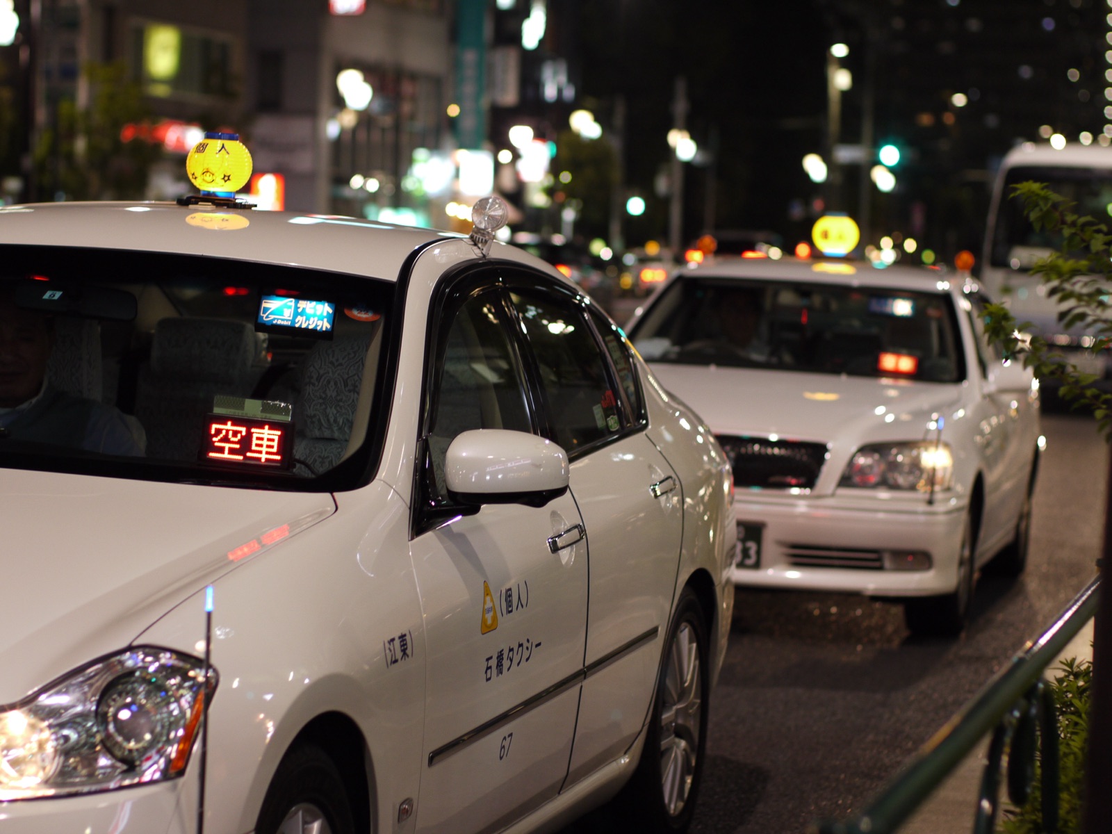 A Tokyo taxi at the curb with the red 空車 (vacant, for-hire) sign illuminated on the dashboard